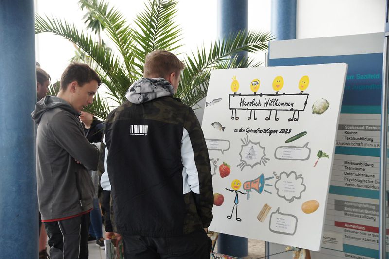 2 Männer schauen auf das Plakat "Gesundheitstag 2023"
