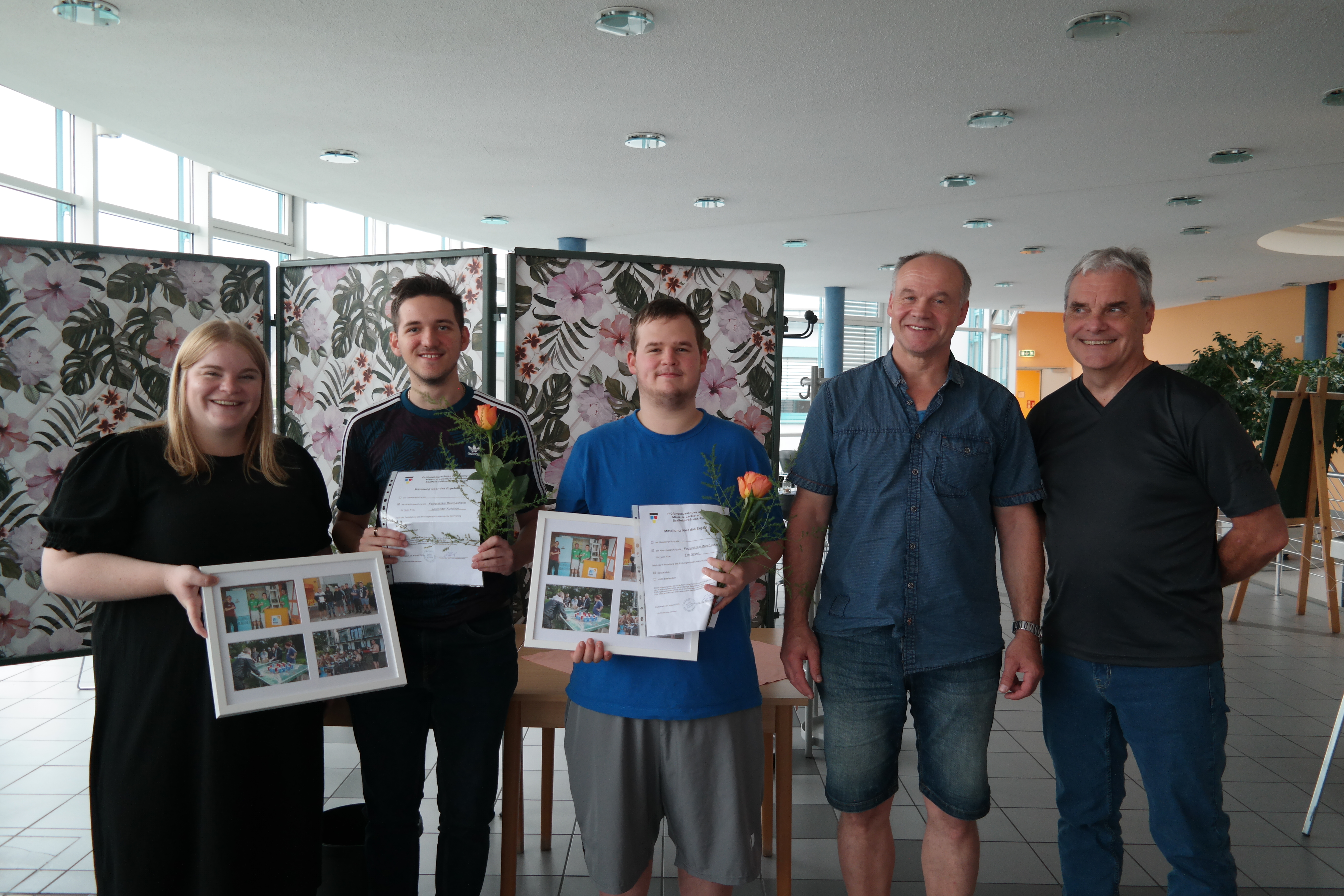 zwei Azubis mit Zeugnissen und drei Ausbilder